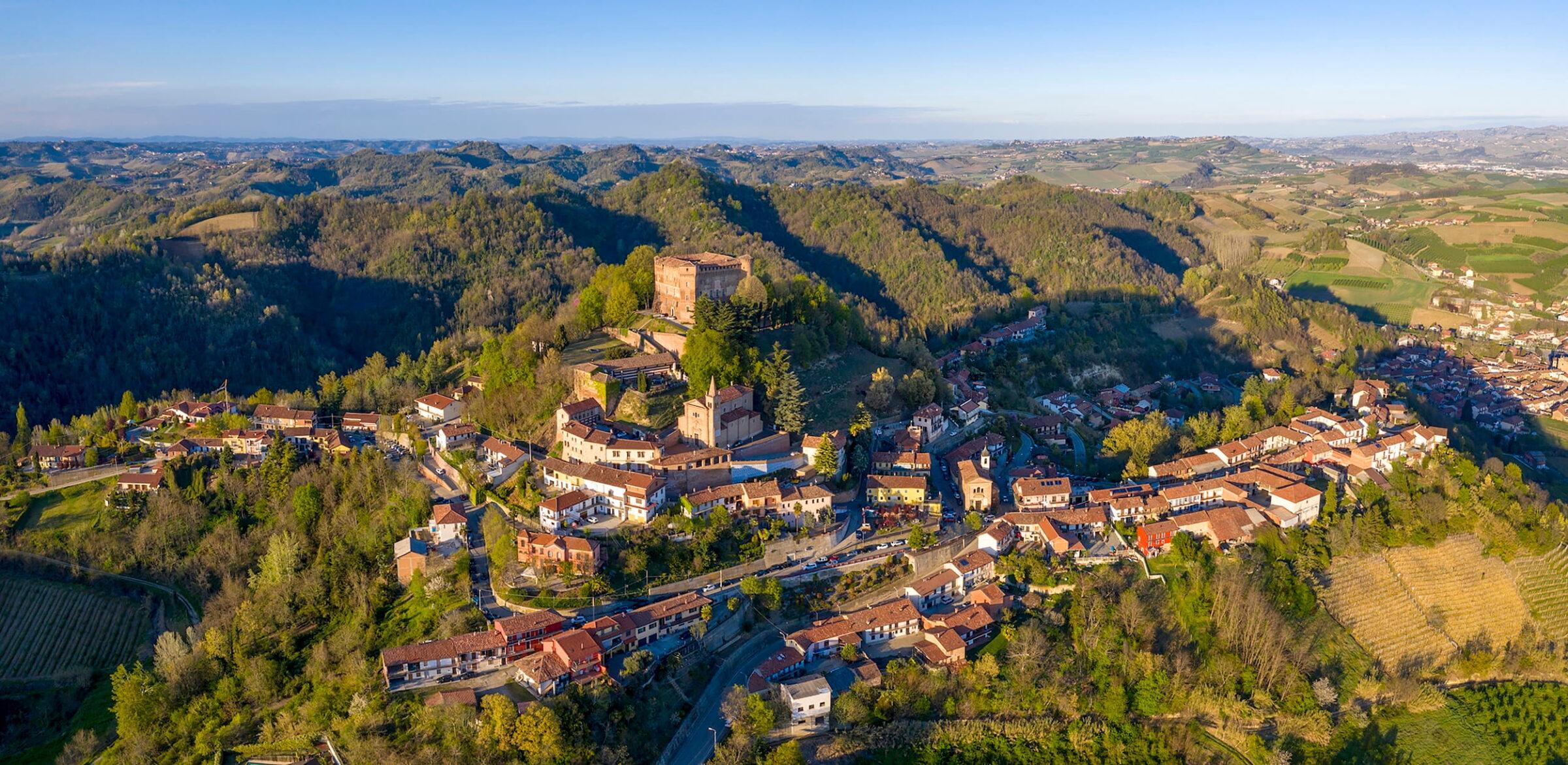 Aerial view of a historic castle complex and a village in the rolling countryside of the Piedmont region